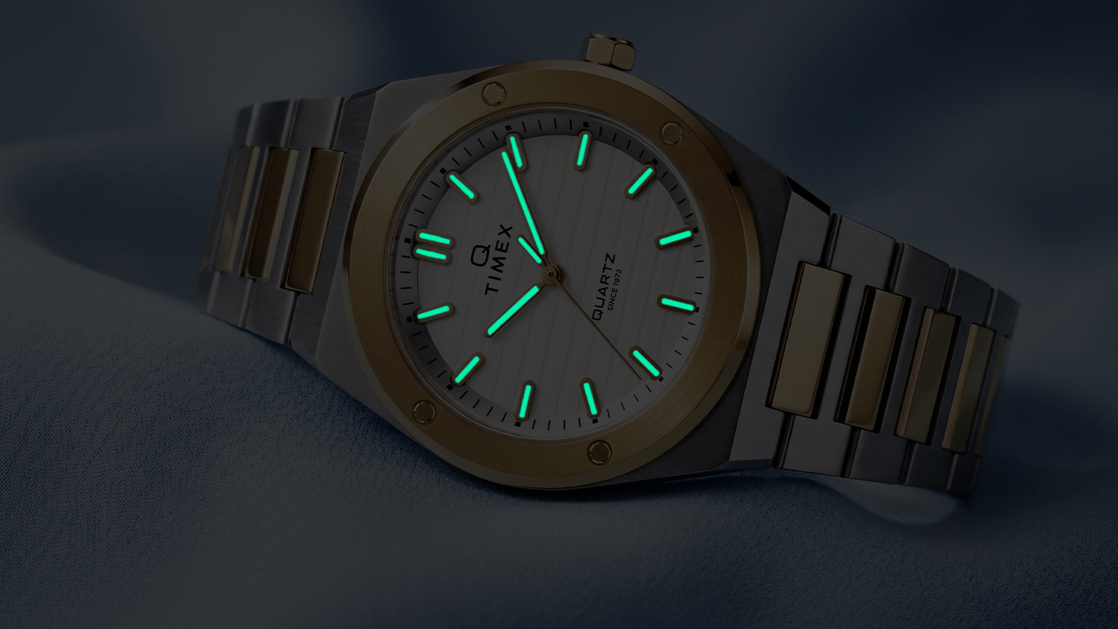 Angled view of the Q Timex Marbella two-tone watch showcasing illuminated Indiglo® hands and hour markers.