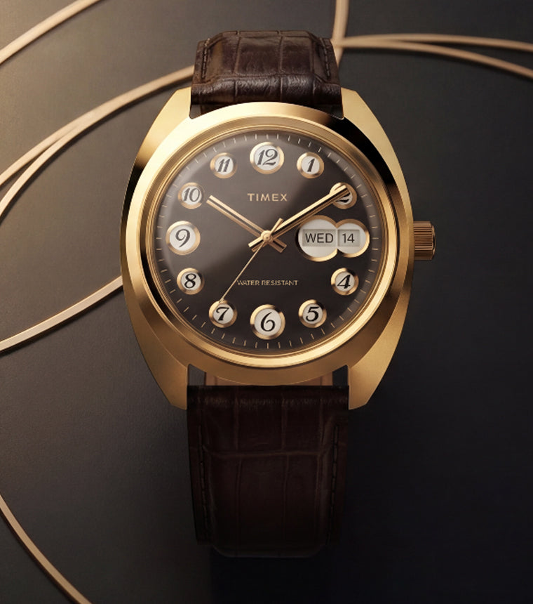 Timex® 1976 Rotary Phone Dial Reissue watch with a gold-tone case, black dial and brown leather strap surrounded by curved gold lines.