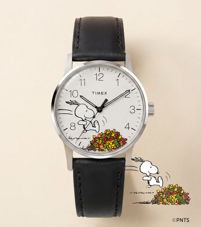 Peanuts® x Timex Waterbury Classic watch with a white dial, black leather strap, and Snoopy running toward a colorful pile of autumn leaves.