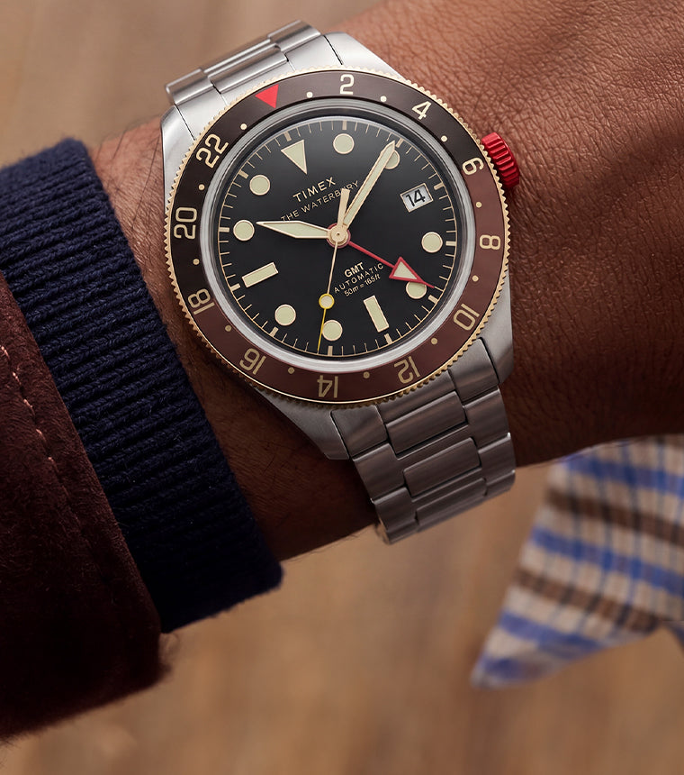 Close-up of the Waterbury Heritage Automatic GMT watch worn on the wrist with layered brown and navy sleeves.
