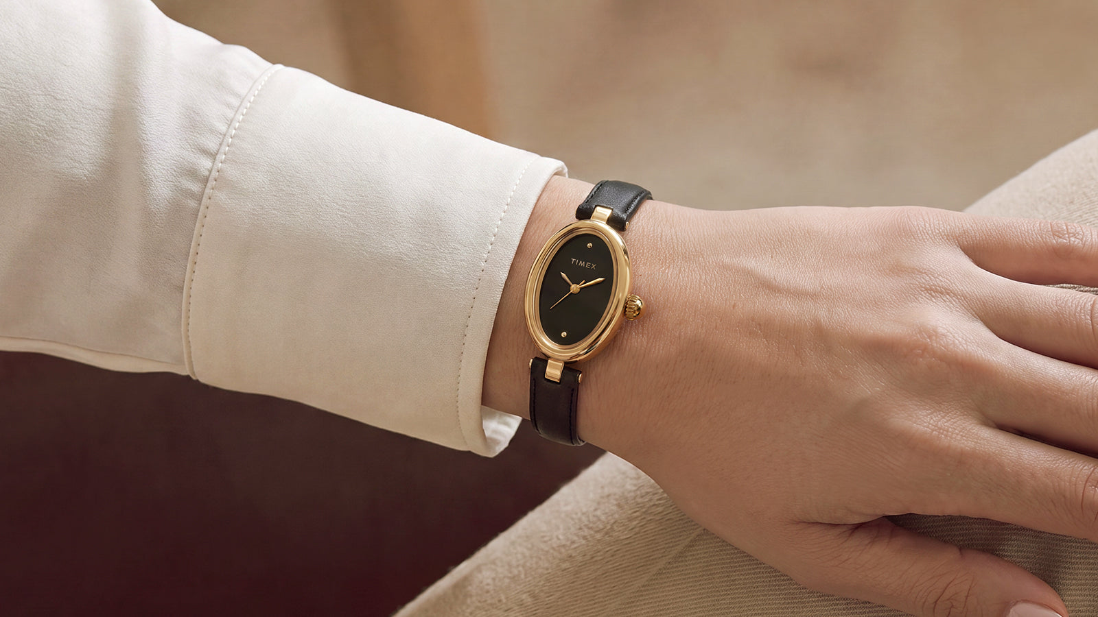 Timex Cavatina® Luxe gold-tone watch with a black dial and black leather strap worn on the wrist with a cream-colored sleeve.