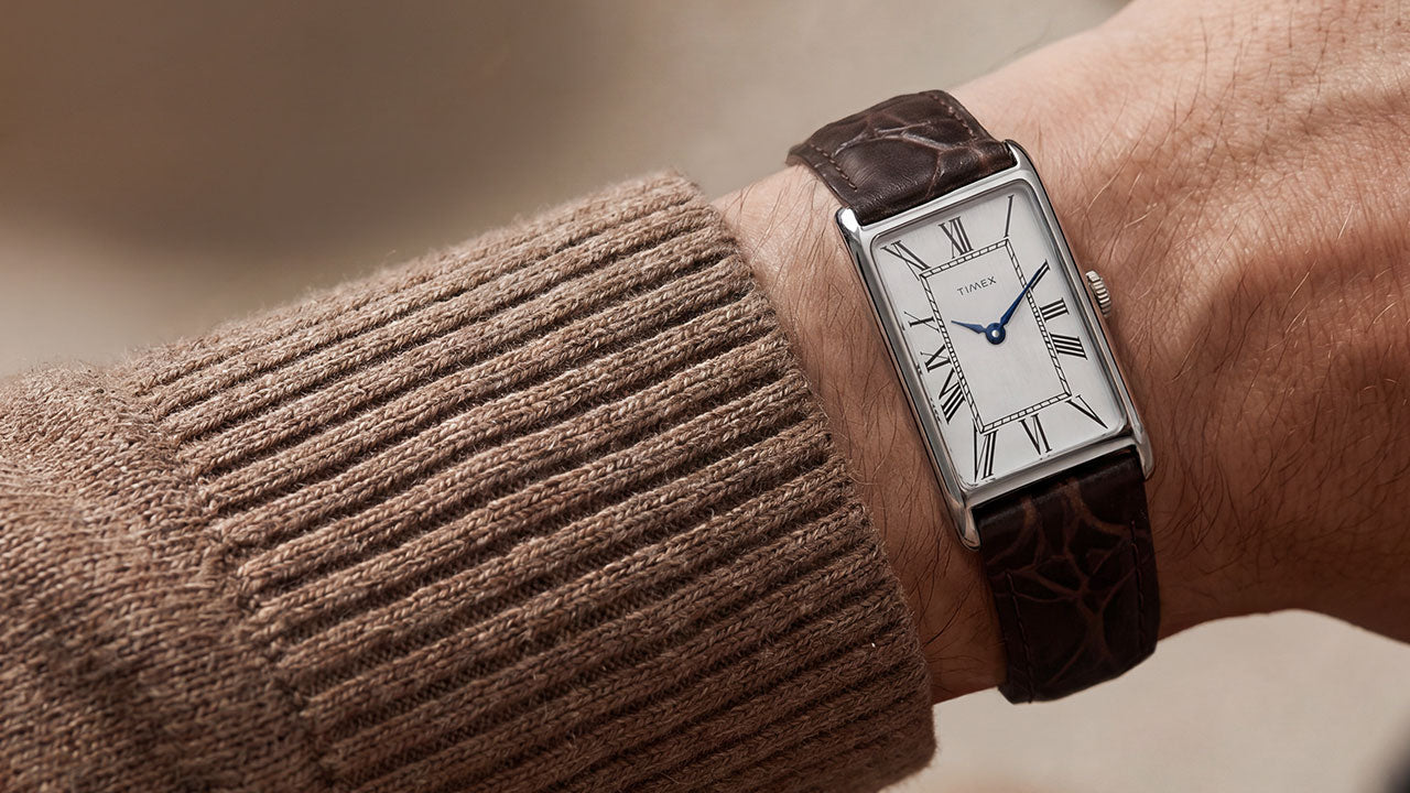 Timex 1976 Lexington Reissue Inspired watch worn on the wrist, featuring a silver sunray dial with Roman numerals, blue hands, and a brown crocodile-grain leather strap.