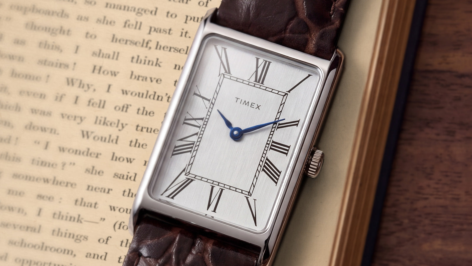 Angled close-up of the Timex 1976 Lexington Reissue Inspired watch with a silver sunray dial, blue hands, Roman numerals, and polished rectangular case.