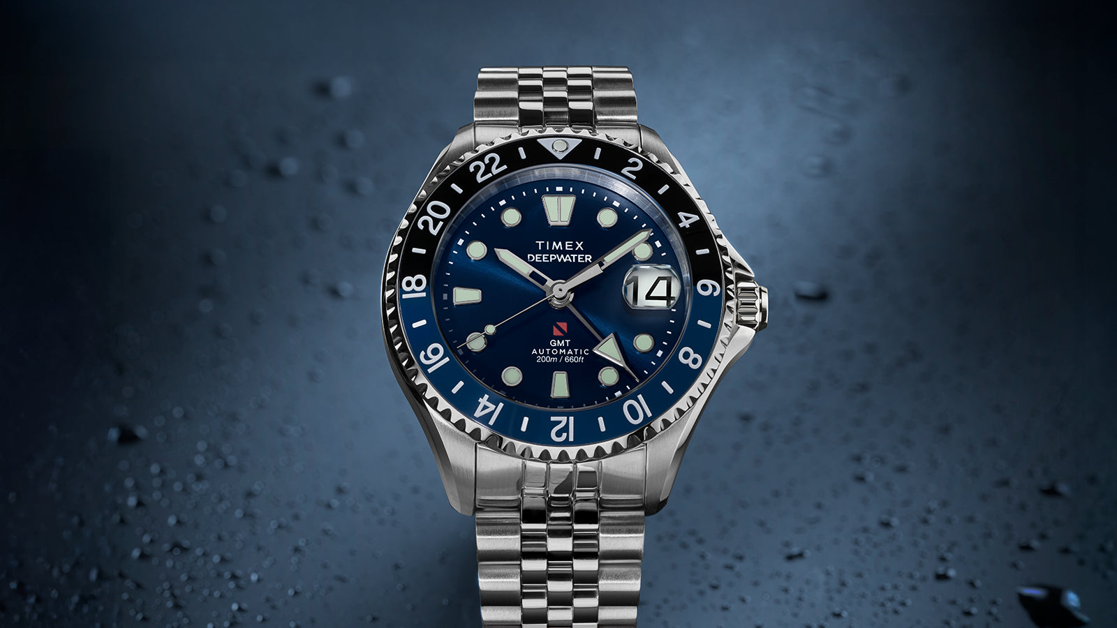 Front-facing view of the Timex Deepwater Meridian 200 Automatic GMT with a blue dial, black-and-blue GMT bezel, magnified date display, and stainless steel bracelet.