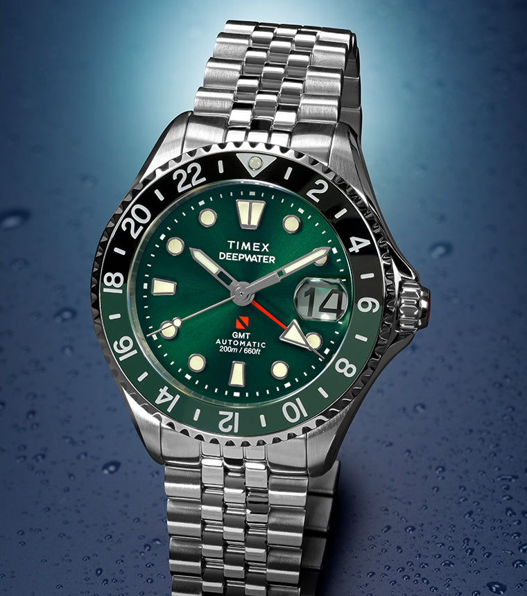Deepwater Meridian 200 Automatic GMT watch with a green dial and matching green 24-hour GMT bezel, stainless steel case and jubilee-style bracelet, date magnifier at 3 o’clock, displayed against a dark blue water droplet background.
