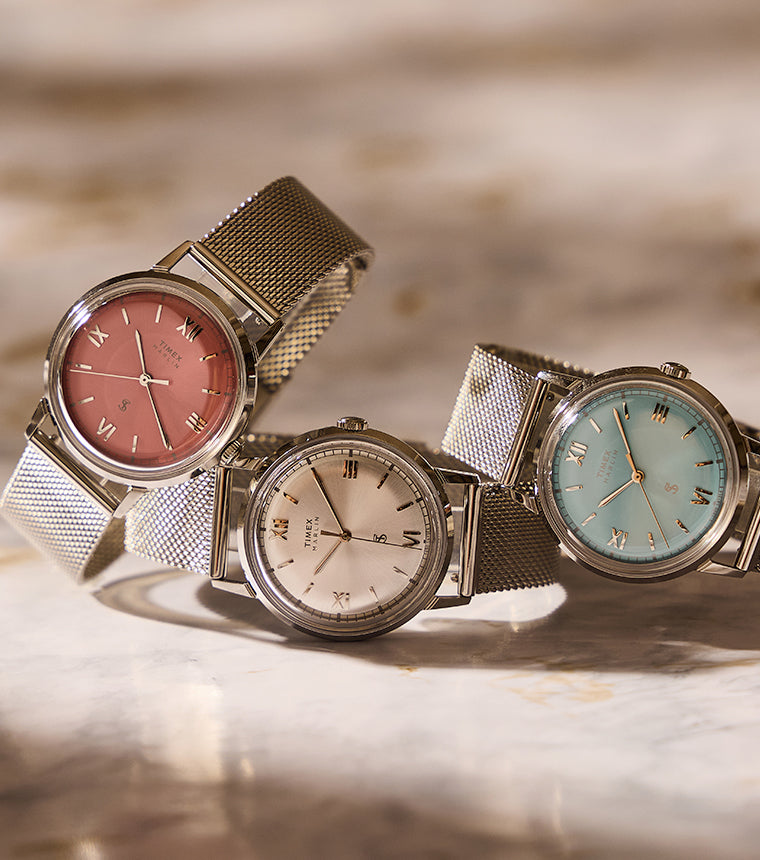Todd Snyder x Timex Marlin® Mesh watches with pink, silver, and light blue dials and stainless steel mesh bracelets displayed together on a marble surface.