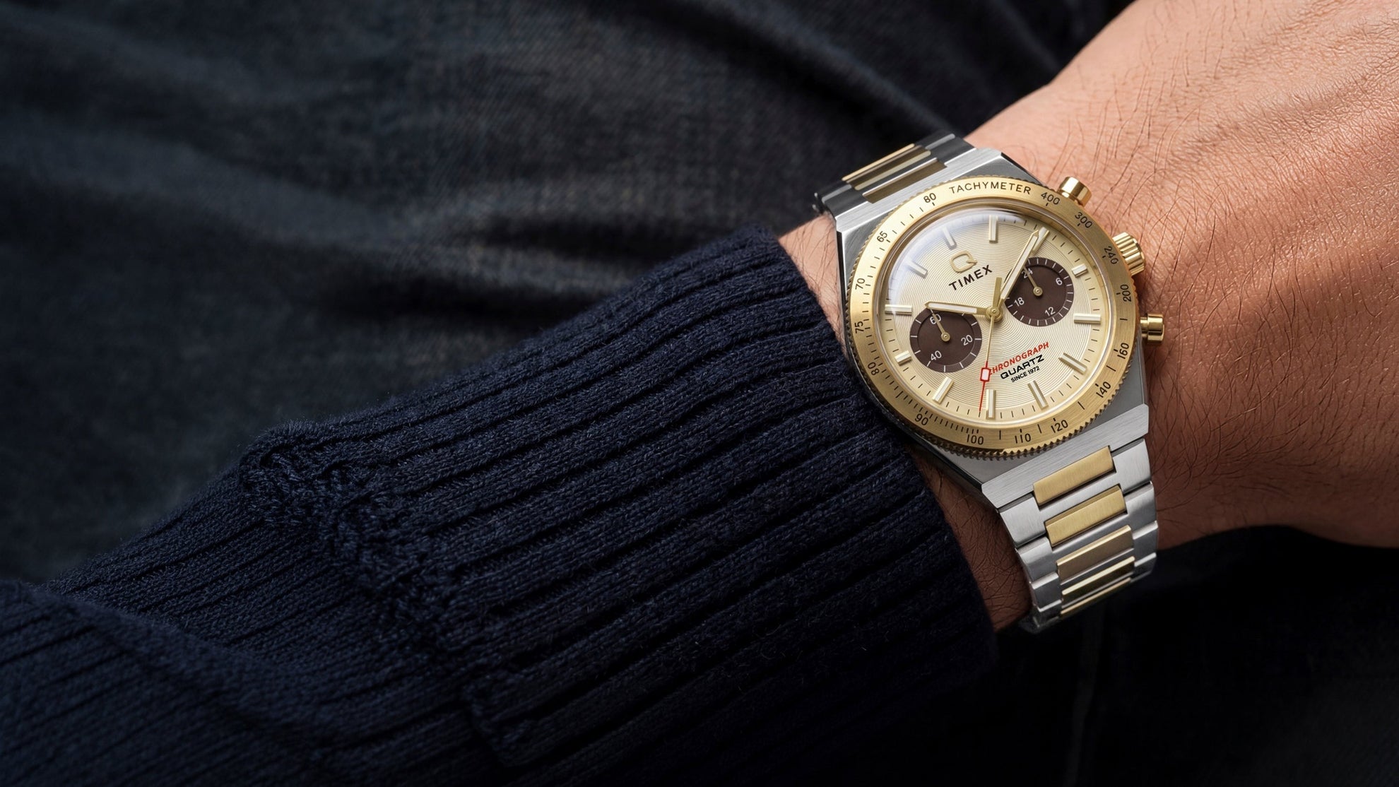 Q Timex Continental Chronograph worn on the wrist with a navy sweater, featuring a two-tone bracelet and champagne chronograph dial.