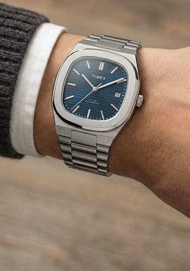 Close-up of the Timex® Automatic E Line 38mm stainless steel watch with a blue textured dial and date window worn on the wrist.