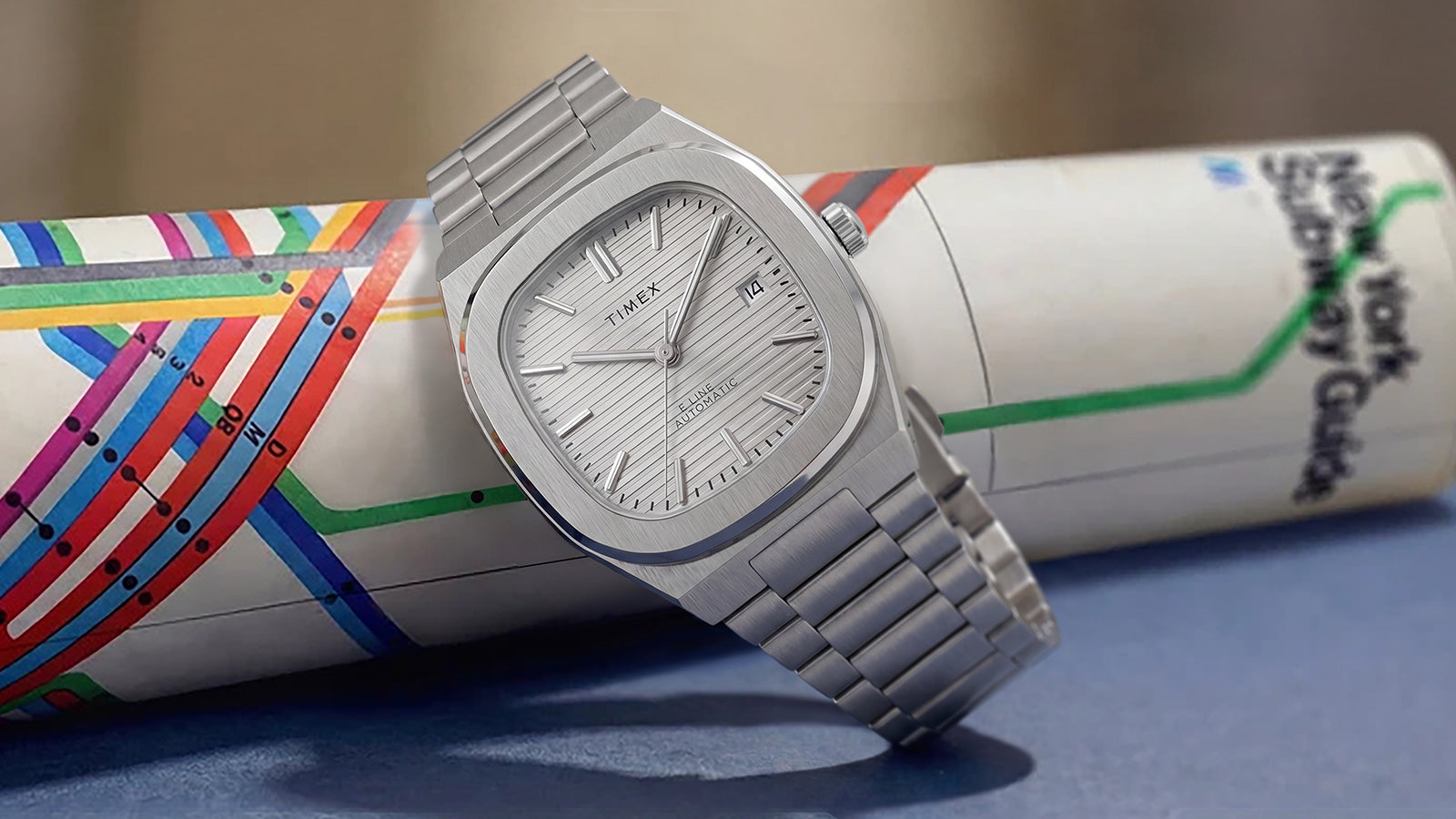 Timex® Automatic E Line 38mm stainless steel watch with a silver textured dial displayed on a rolled New York City subway map.