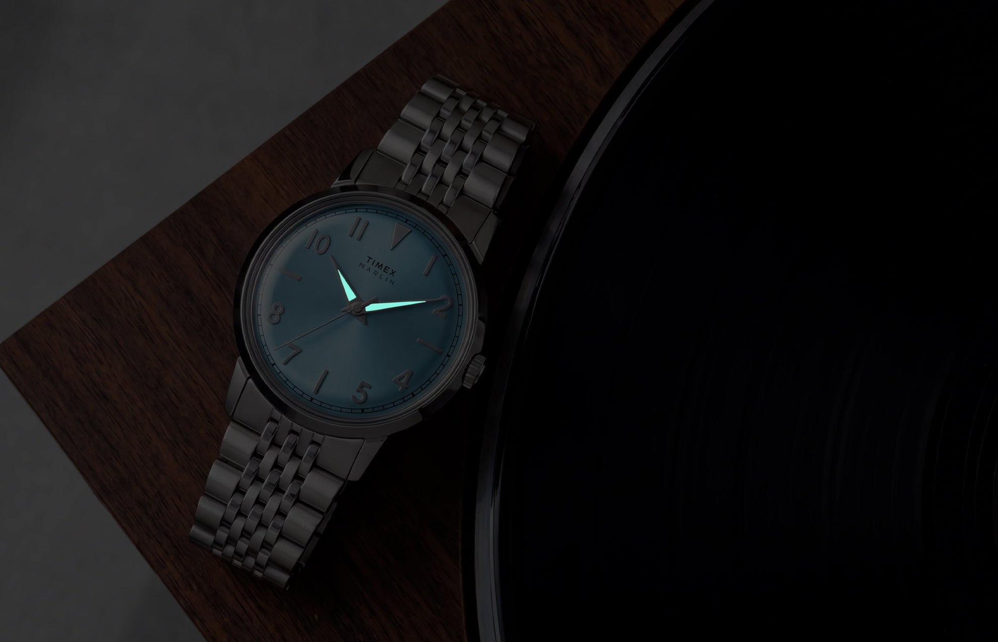 Timex Marlin Quartz watch with luminous hands glowing in low light beside a vinyl record.