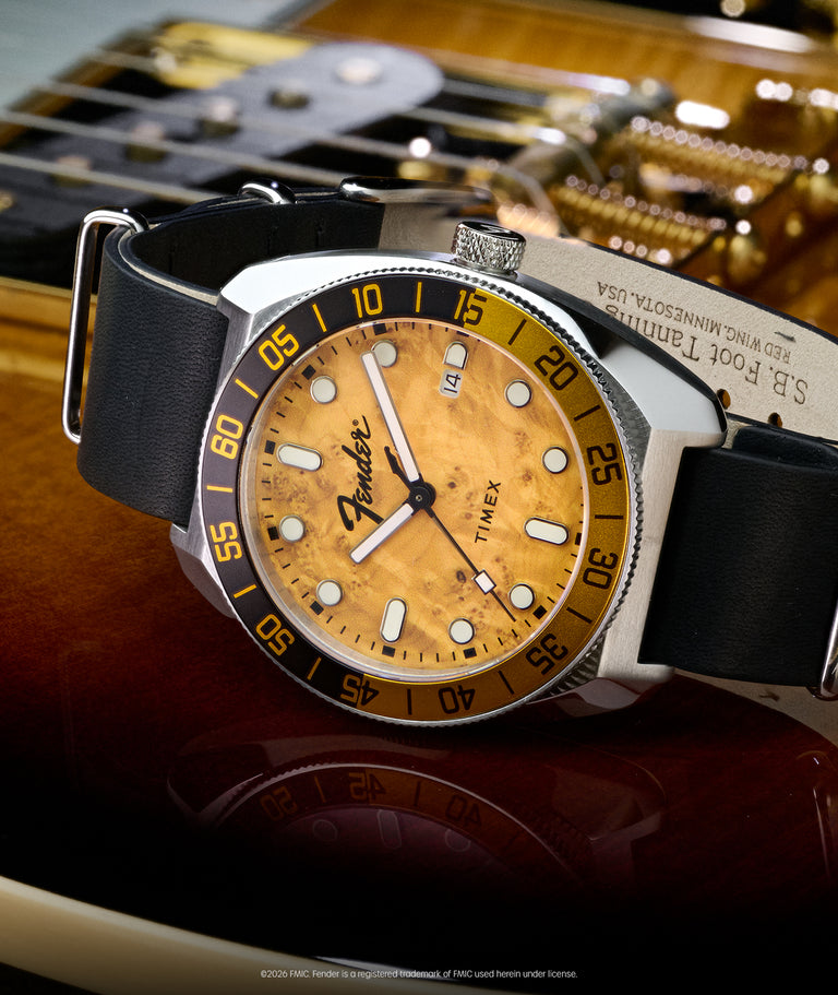 Fender x Timex Automatic watch with a wood-grain dial, black strap, silver-tone case, and rotating bezel displayed on a Fender guitar.