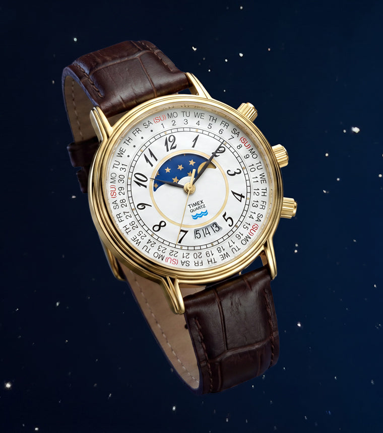 Timex 1990 Moon Phase and Calendar Dial Reissue with a gold-tone case, white calendar dial, moon phase display, and brown leather strap against a starry blue background.