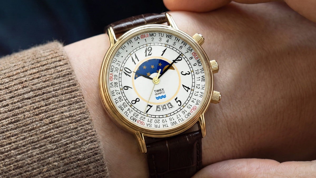Timex 1990 Moon Phase and Calendar Dial Reissue worn on the wrist with its gold-tone case, white dial, and brown leather strap in view.