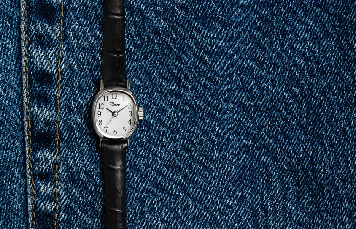 Cavatina® Mini watch with a silver-tone case, white dial, and black leather strap displayed on blue denim.
