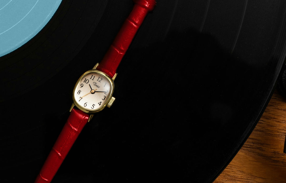 Cavatina® Mini watch with a gold-tone case, champagne dial, and red leather strap displayed on a vinyl record.