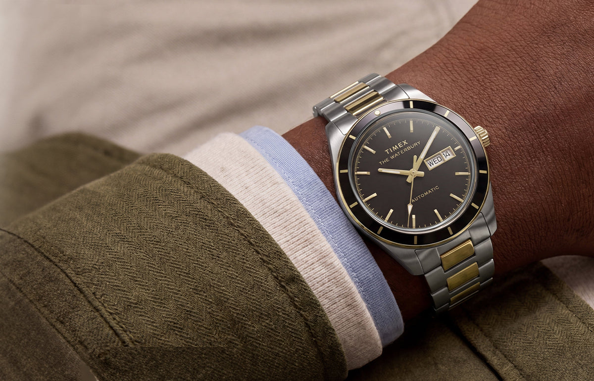 Close-up of the two-tone Waterbury Heritage Automatic watch worn on a wrist, featuring a black dial and day-date window.