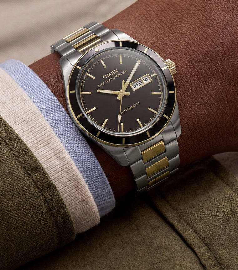 Close-up of the two-tone Waterbury Heritage Automatic watch worn on a wrist, featuring a black dial and day-date window.