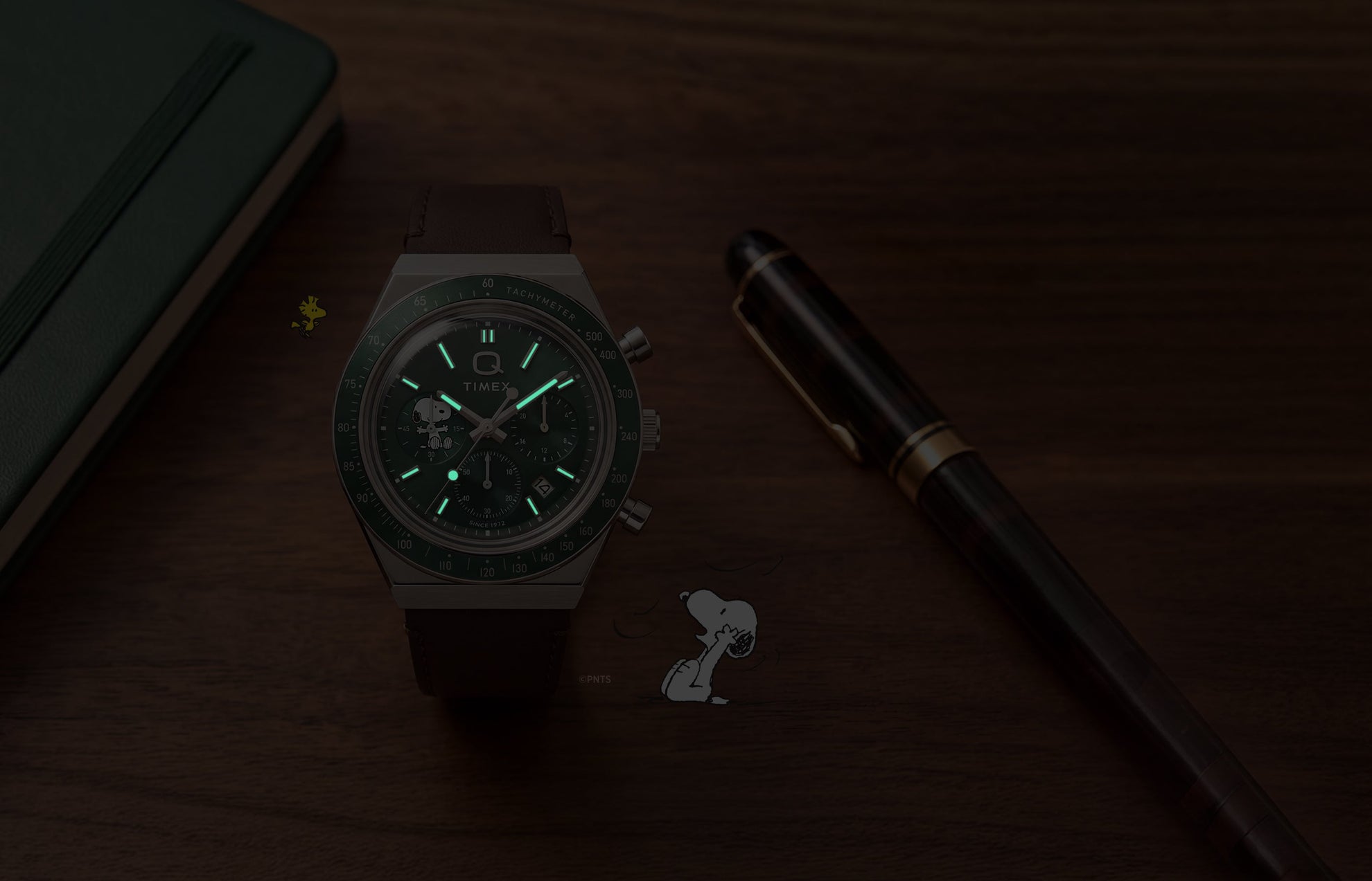 Peanuts® x Q Timex Chronograph shown in low light with glowing hands and hour markers.