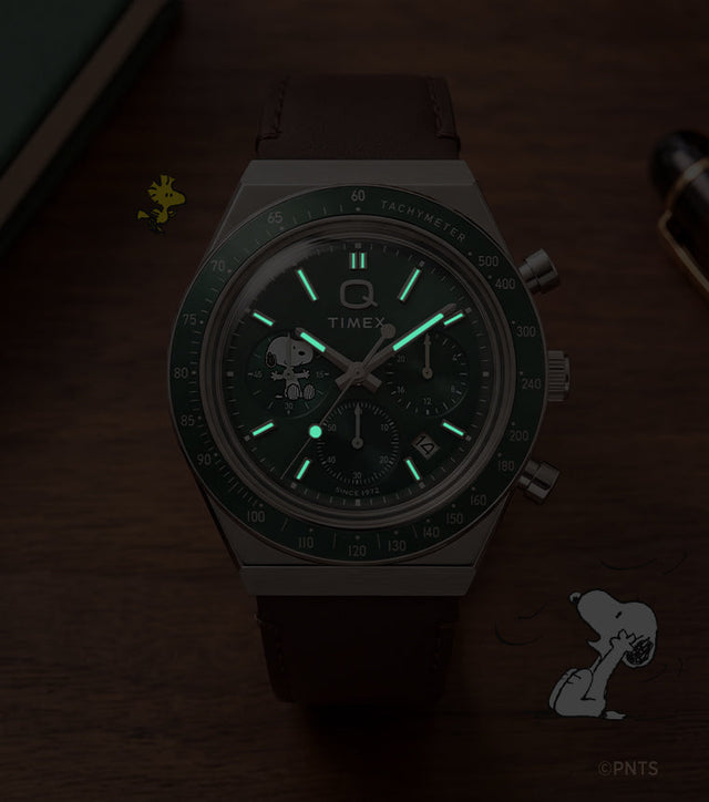 Peanuts® x Q Timex Chronograph shown in low light with glowing hands and hour markers.