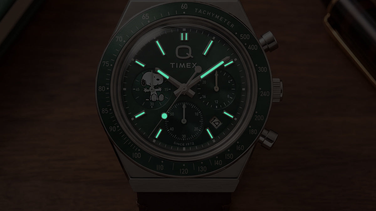Close-up of the Peanuts® x Q Timex Chronograph dial in low light, highlighting its luminous hands and hour markers.