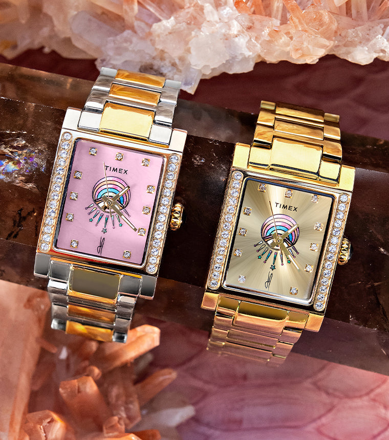 Two Timex x Jacquie Aiche Éclat watches with pink and champagne eye-motif dials displayed among pink crystals.