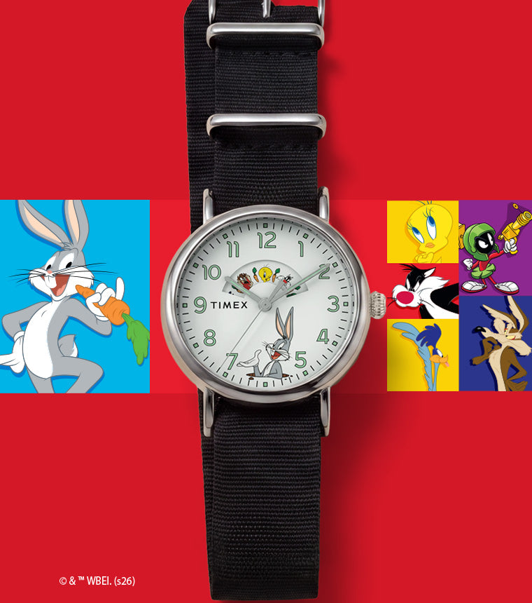 TW2Y99100 Looney Tunes Bugs and Friends x Timex Standard watch with a white character dial and black fabric strap beside colorful Looney Tunes artwork.