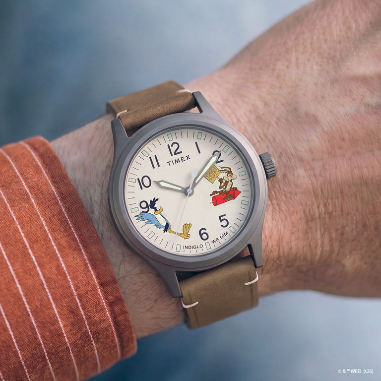 TW2Y99400 Road Runner & Wile E. Coyote x Timex Expedition® Scout watch worn on a wrist, featuring a cream dial, gray case, and brown leather strap.