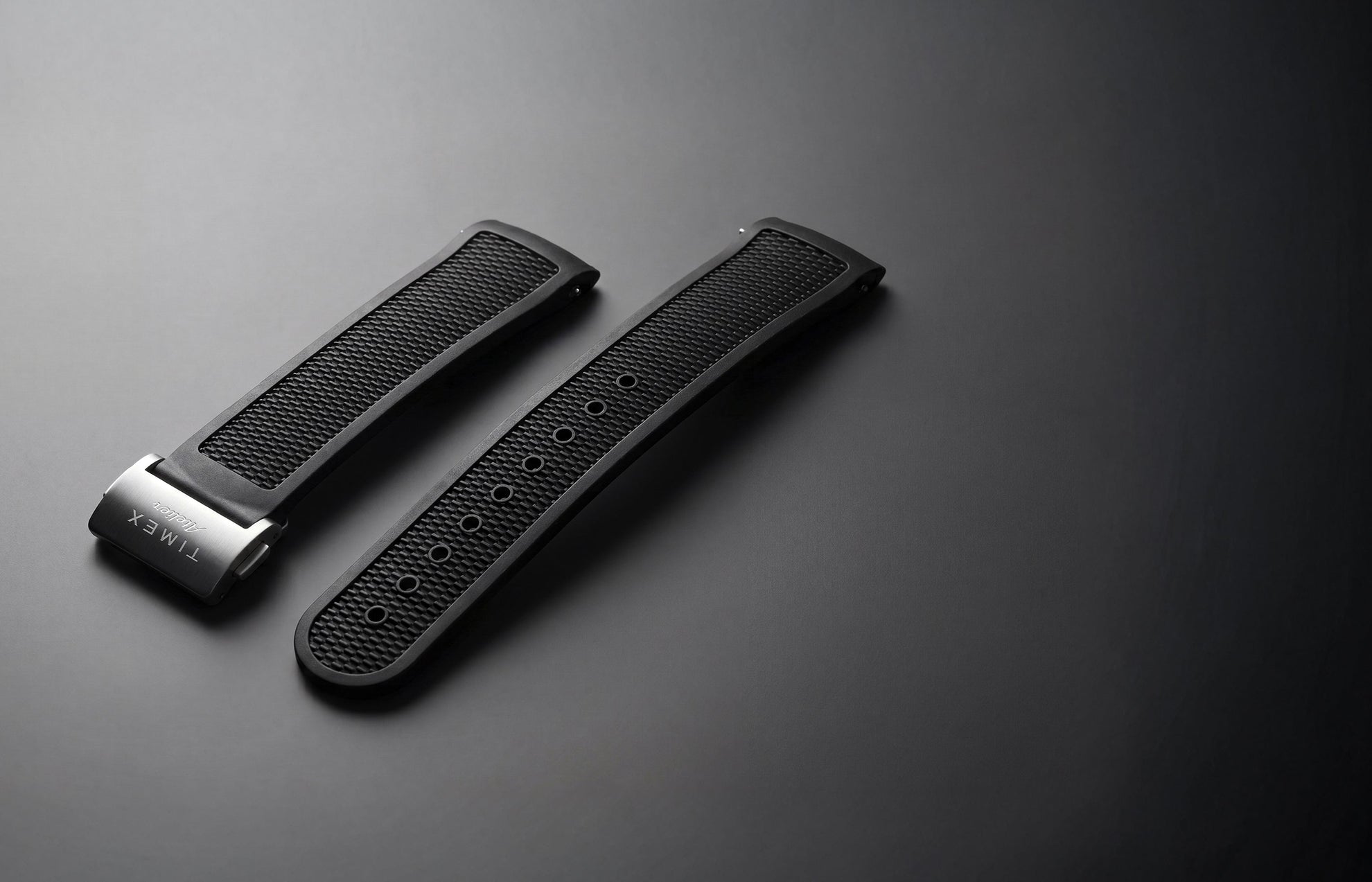 Timex Atelier NBR synthetic rubber strap in black with a textured finish and stainless-steel clasp, displayed against a dark background.