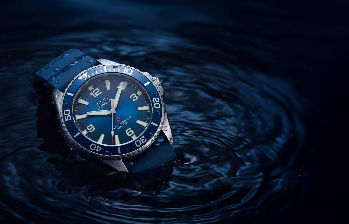 TW3A01900 Deepwater Arctic 200 watch with a blue dial and strap resting in dark, rippling water.