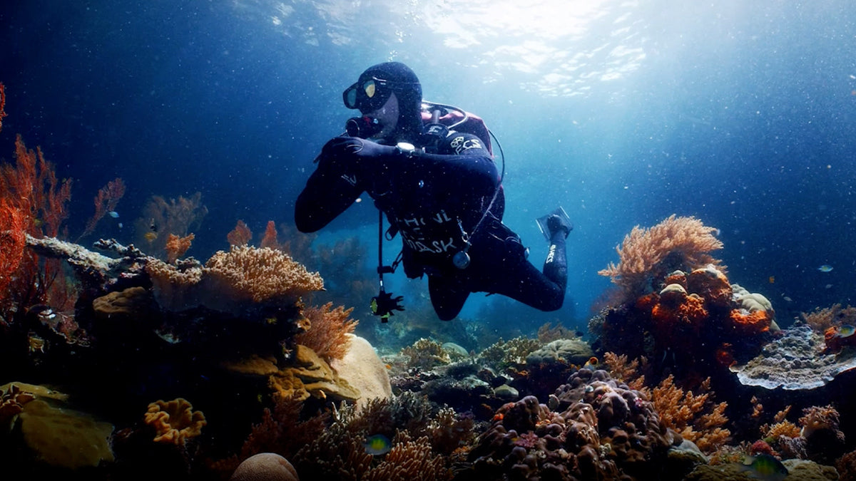 TW3A01900 Scuba diver swimming above a colorful coral reef in clear blue water.