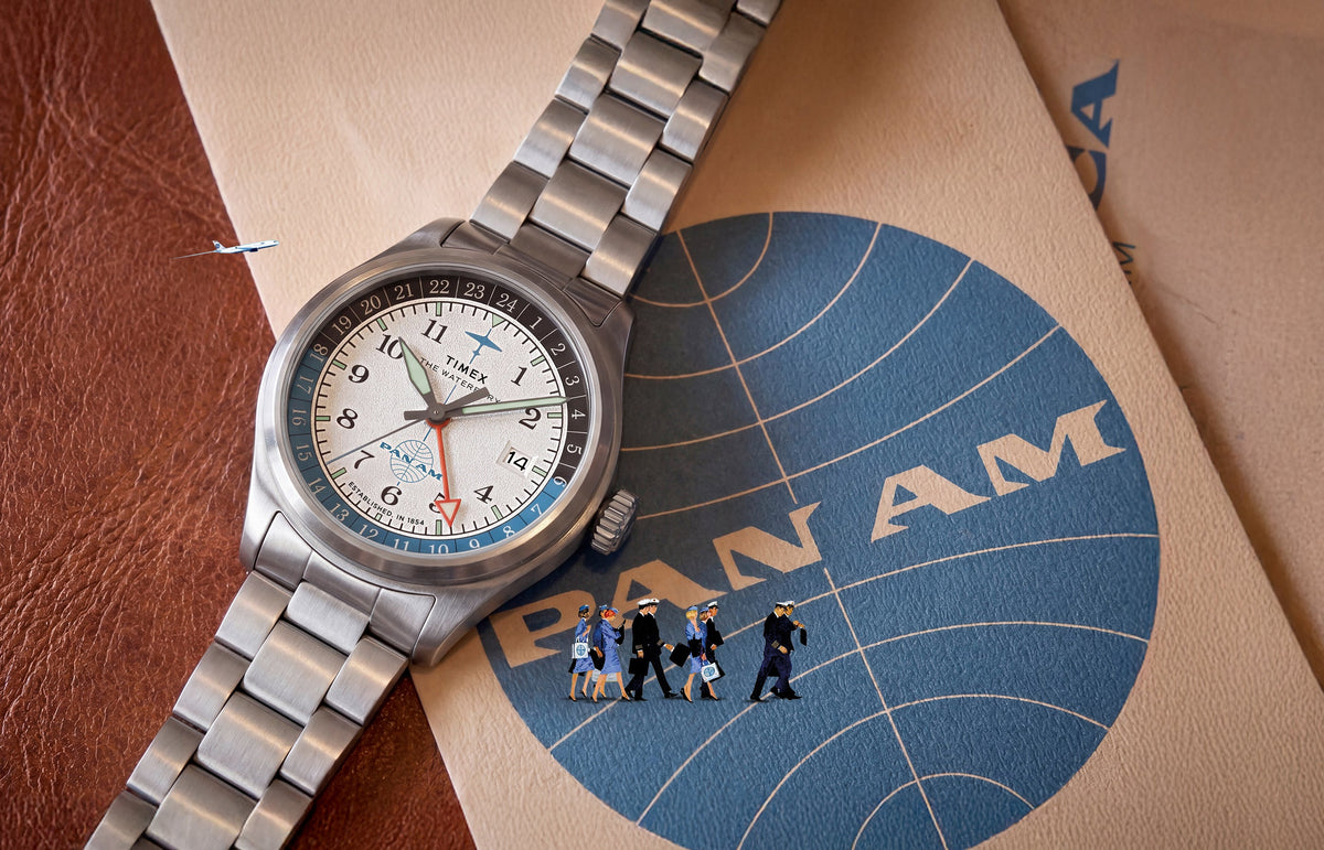 TW2Y94600 Pan Am x Timex Waterbury Automatic GMT watch displayed on vintage Pan Am materials with miniature airline crew and airplane details.
