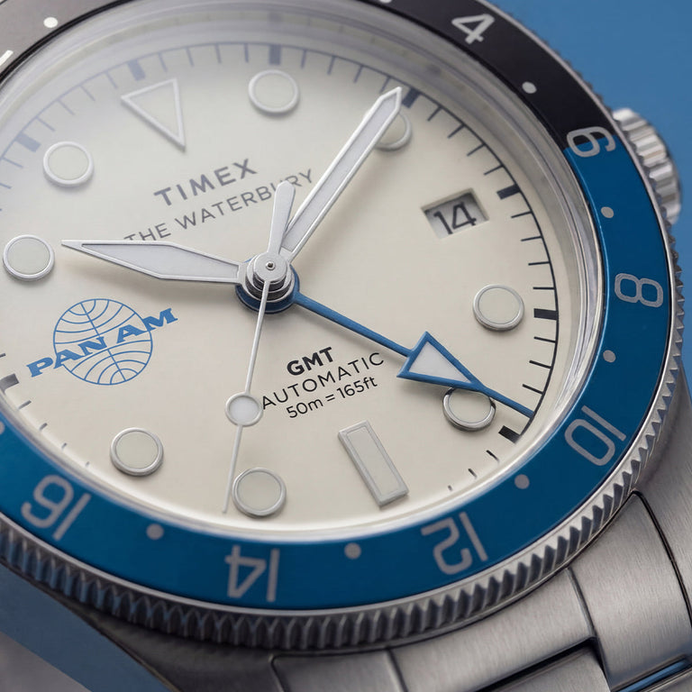 TW2Y94300 Macro view of the cream dial with the Pan Am logo, blue GMT hand, date window, and blue-and-black bezel.