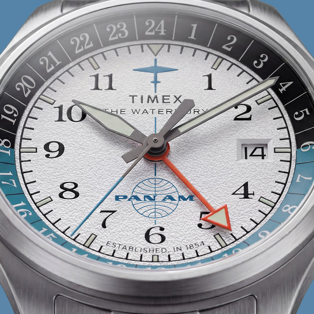 TW2Y94600 Macro view of the textured white dial with black numerals, Pan Am logo, orange GMT hand, and date window.