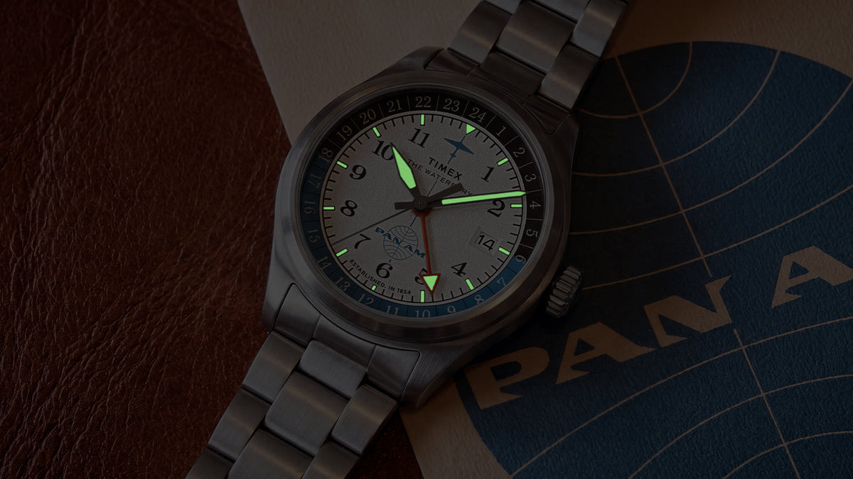 TW2Y94600 Pan Am x Timex Waterbury Automatic GMT watch glowing beside vintage Pan Am materials.