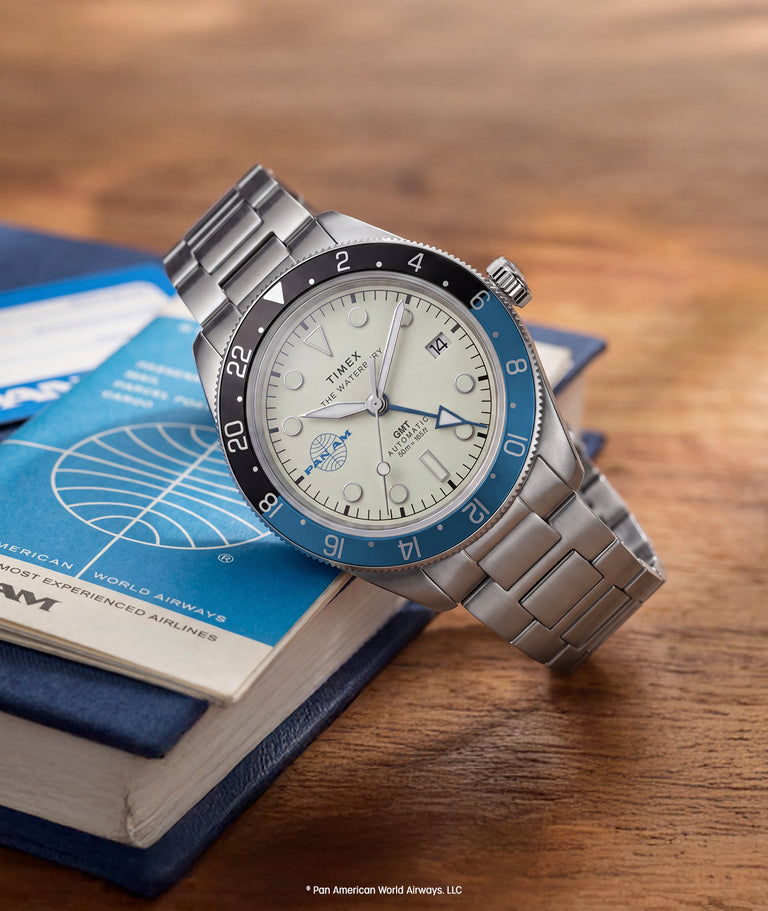 TW2Y94300 Pan Am® x Timex® Waterbury GMT watch with a cream dial, blue-and-black bezel and silver-tone bracelet resting on a Pan Am booklet