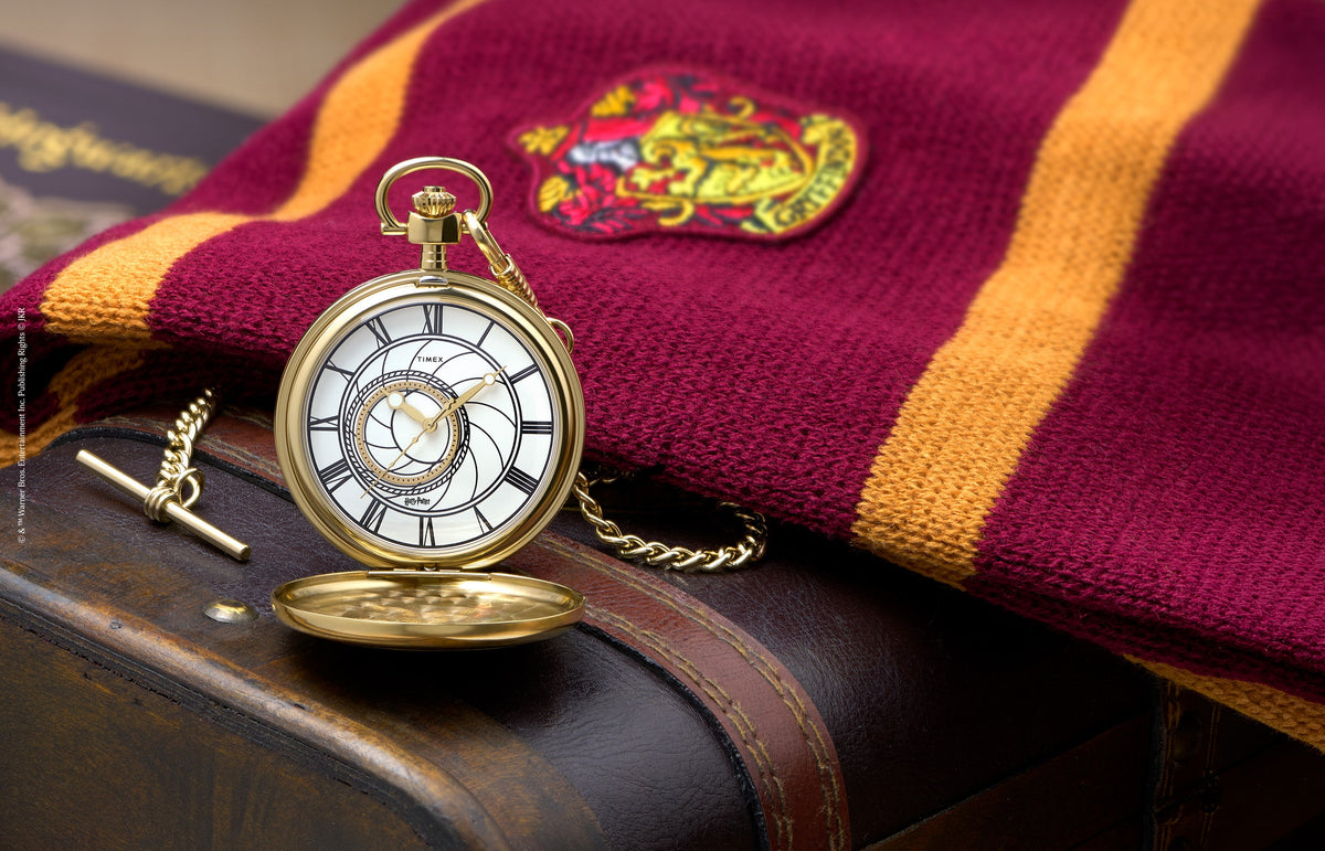 TW2Y99600 Open gold-tone pocket watch with a white Roman numeral dial and chain, displayed beside a burgundy and gold Gryffindor scarf.