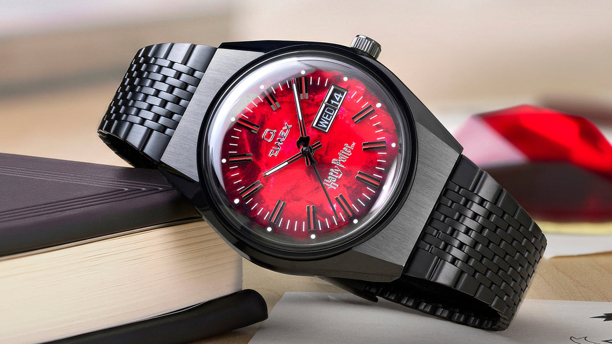 TW2Y99700 Harry Potter x Q Timex watch with red textured dial and black bracelet displayed beside a book and red stone.