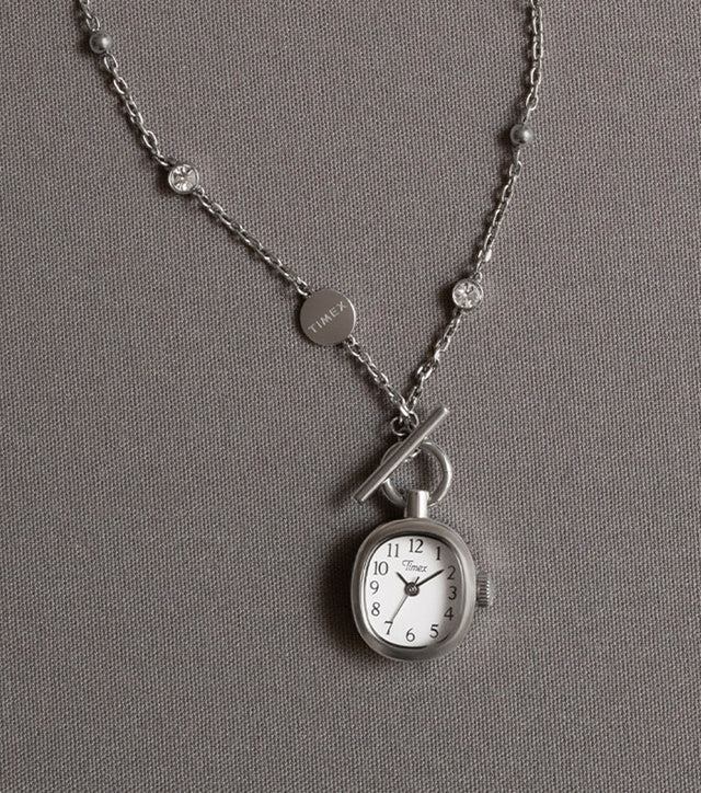 TW6A17600 Cavatina® Mini necklace with an oval white-dial watch pendant and silver-tone chain with clear stones, displayed on gray fabric.