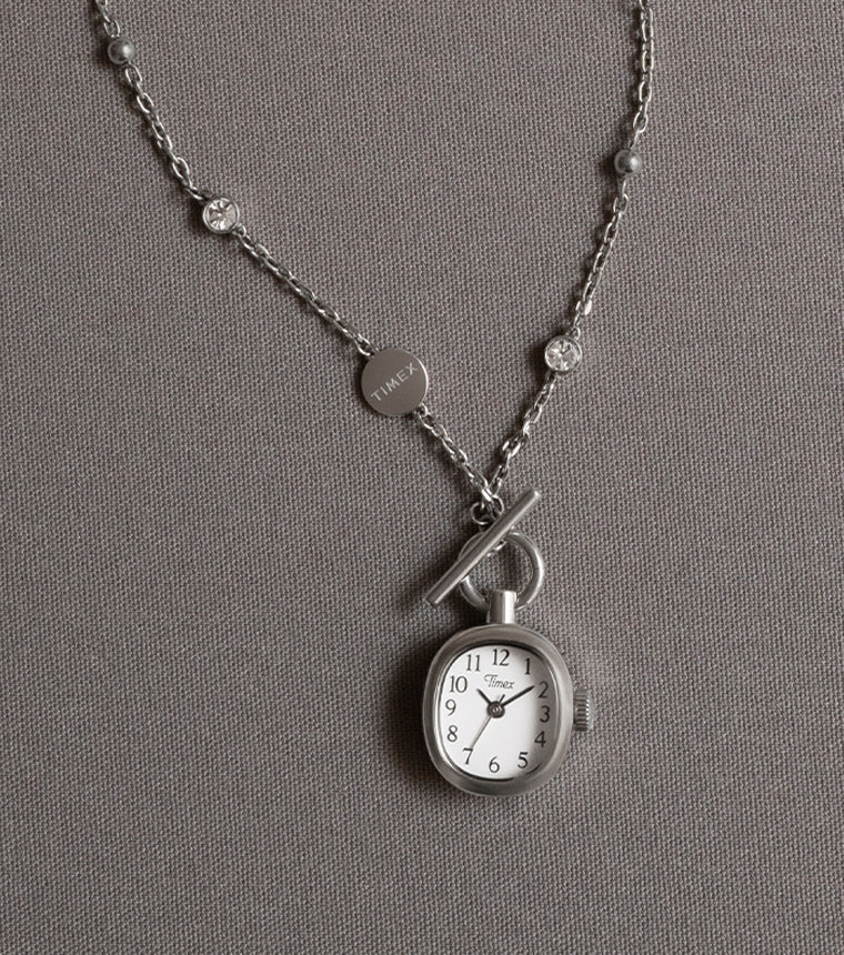 TW6A17600 Cavatina® Mini necklace with an oval white-dial watch pendant and silver-tone chain with clear stones, displayed on gray fabric.