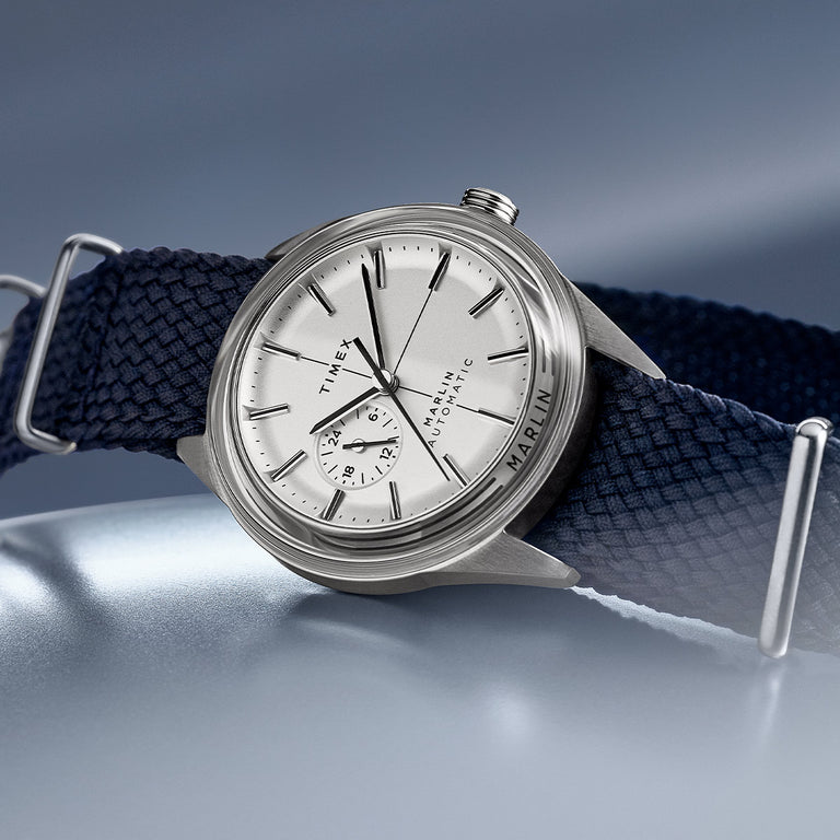 Close-up of the Timex Marlin Automatic watch with a silver-tone dial and case, 24-hour subdial, and navy woven fabric strap.