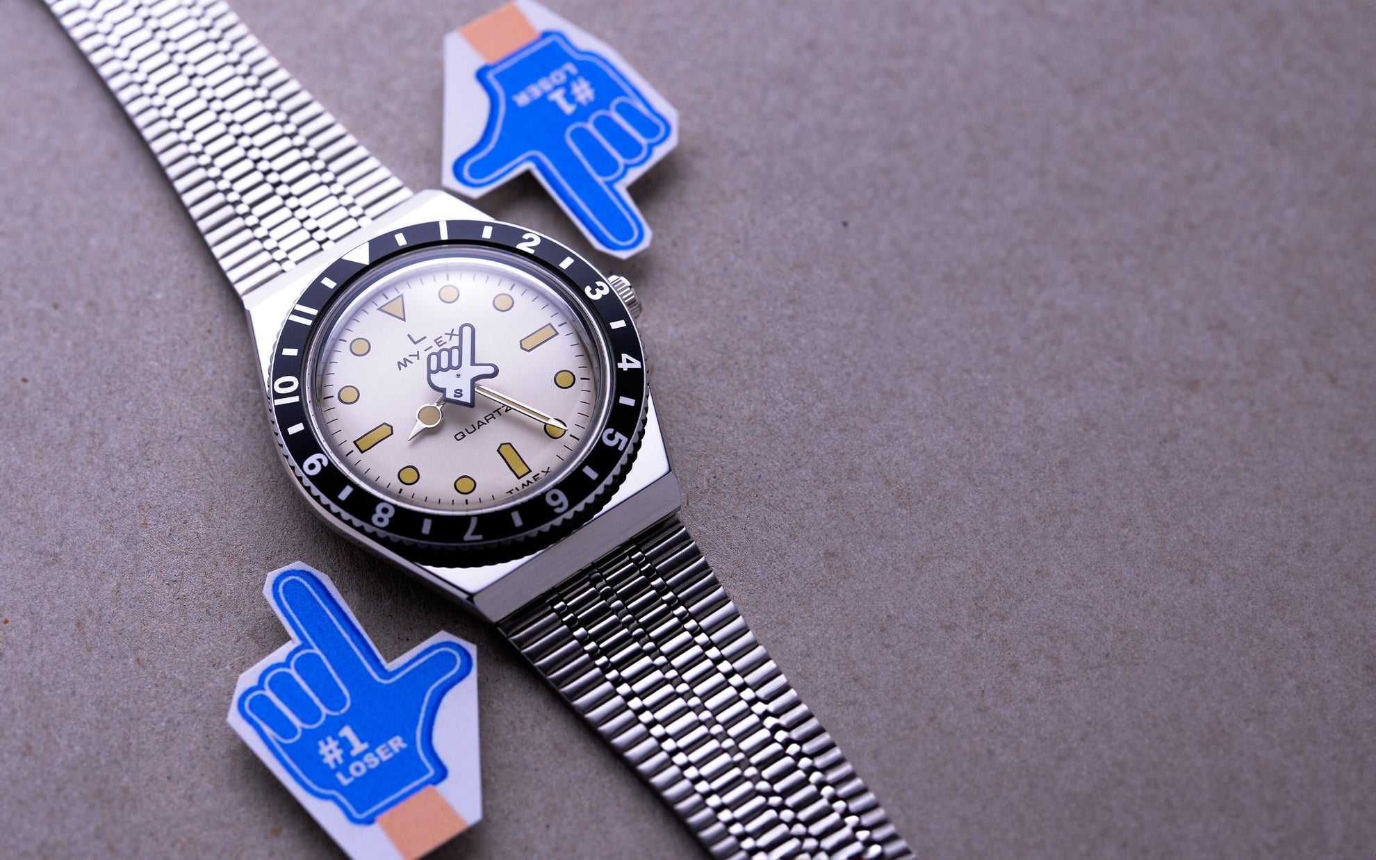 Silver seconde/seconde watch on a grey background with blue hand icons either side