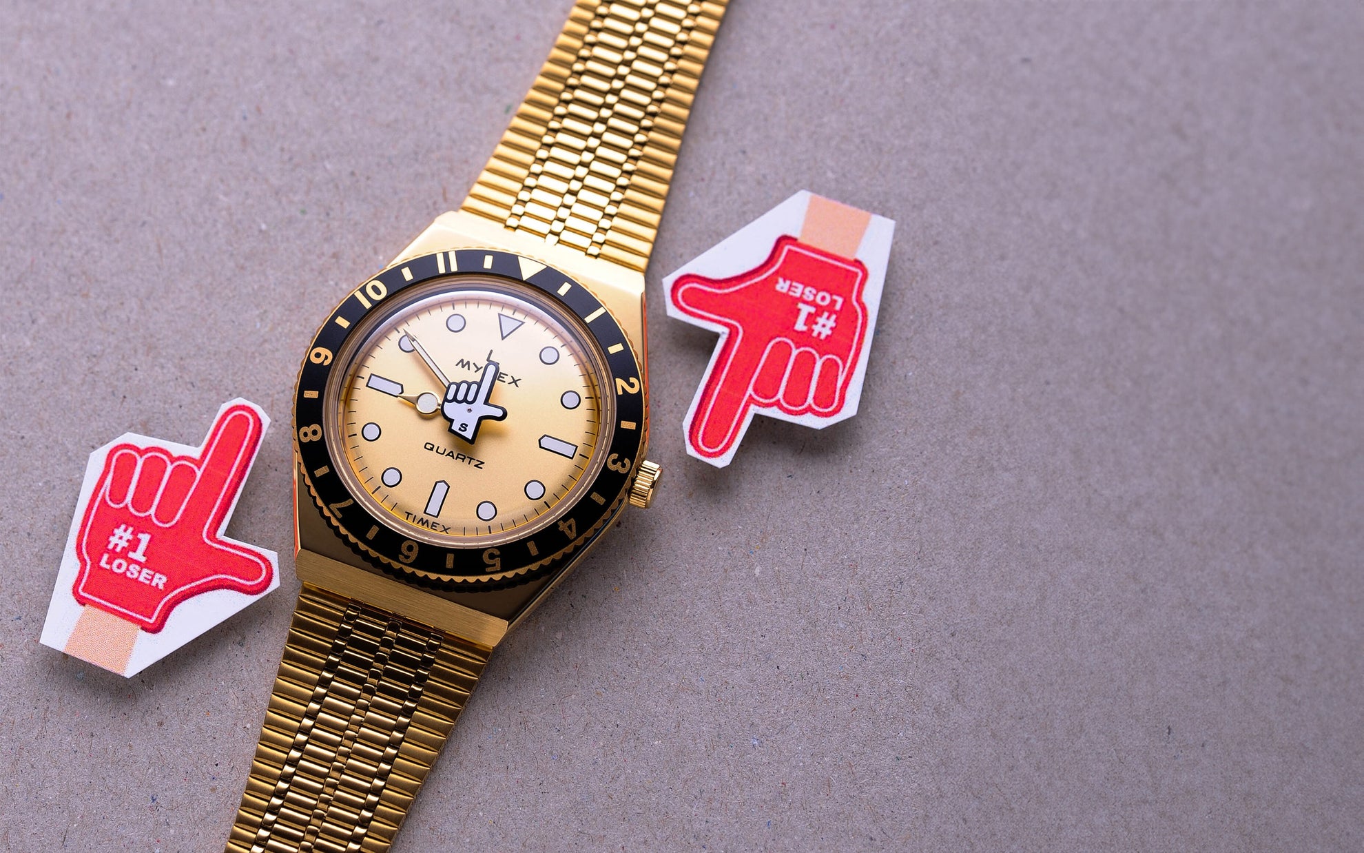 Gold seconde/seconde watch on a grey background with red hand icons either side