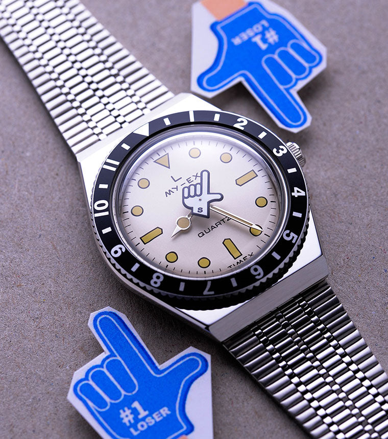 Silver seconde/seconde watch on a grey background with blue hand icons either side