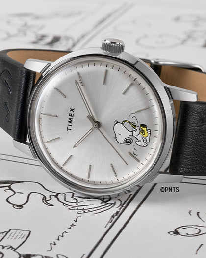 Watch laying on its side over a Snoopy comic. The watch has a black strap and silver dial with Snoopy playing a saxophone icon