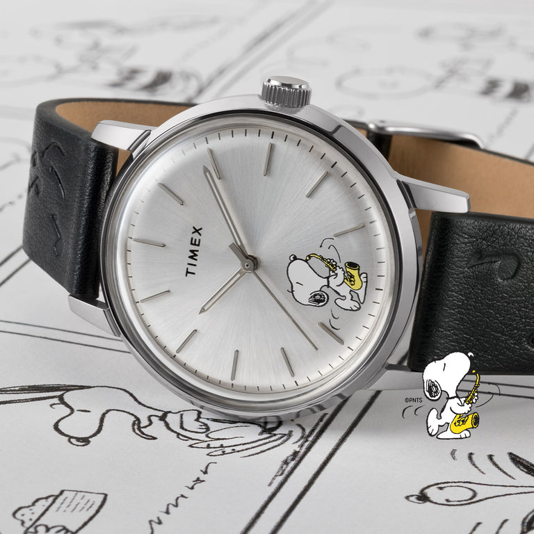 Timex x Peanuts® watch with white dial featuring Snoopy and Woodstock, paired with a green strap on a Peanuts comic background