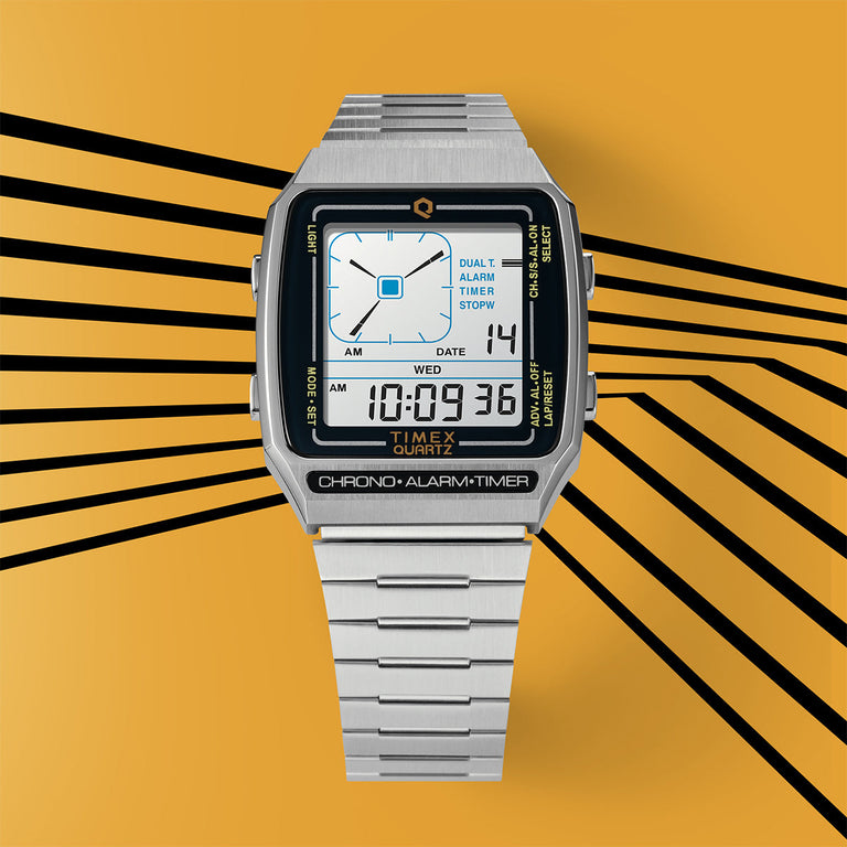 Retro digital Timex Q Reissue watch in stainless steel with a square face. It features a dual time display, alarm, stopwatch, and backlight. Shown against a bold yellow background with graphic black lines.