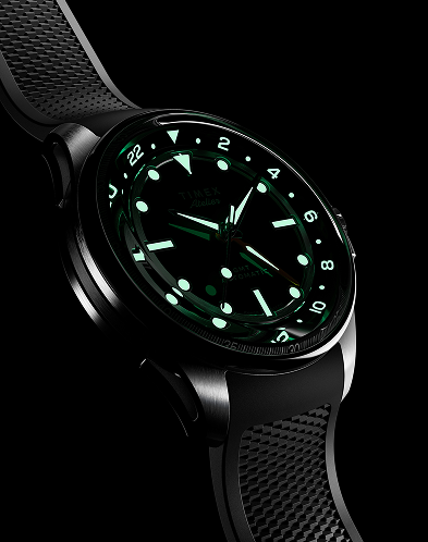 Nighttime image of the Timex Atelier GMT Automatic glowing in green lume, showing its legibility in low light.
