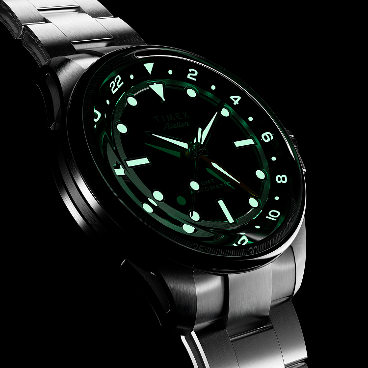 Timex Atelier GMT Automatic glowing in the dark, showing luminous green hour markers and hands.