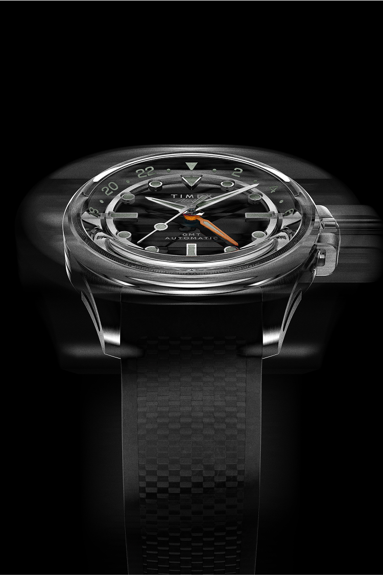 Timex Atelier GMT Automatic with a black dial, orange GMT hand, and black rubber strap shown in motion blur to emphasize precision.