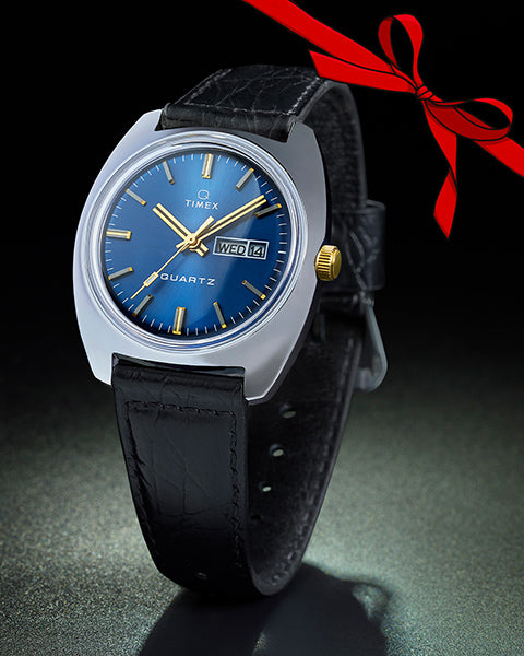 Steel watch with a blue face and gold details with a leather band. There is a red bow in the top right corner.